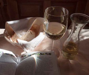 A glass of Italian white wine, some bread and a book all on a table